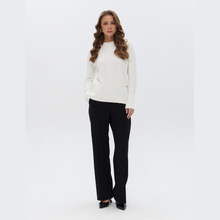 Load image into Gallery viewer, A woman modeling a white cable-knit mock-neck sweater and black wide-leg trousers against a plain white studio background.