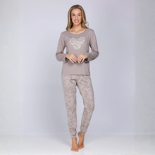 Load image into Gallery viewer, A woman modeling a two-piece pajama set consisting of a long-sleeve top with a white embroidered heart on a taupe-gray background, and matching patterned pants, against a light gray studio backdrop.