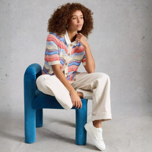 Load image into Gallery viewer, Person sitting on a blue chair wearing a colorful striped cardigan and white pants.
