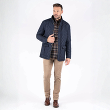 Load image into Gallery viewer, Man wearing a navy quilted jacket over a plaid shirt with beige pants on a white background