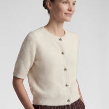 Load image into Gallery viewer, A woman wearing a short-sleeve cream knit cardigan with decorative silver-tone buttons, shown from the waist up against a light gray studio background.