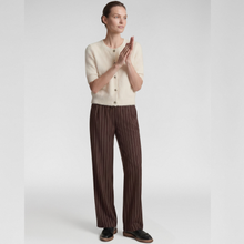 Load image into Gallery viewer, A model stands against a light gray studio background wearing a cream short-sleeve button-front cardigan and dark brown wide-leg trousers with thin vertical pinstripes, paired with black shoes.