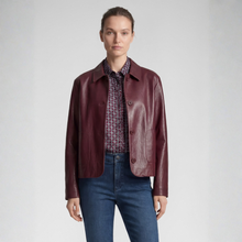 Load image into Gallery viewer, A model wearing a cropped, dark burgundy leather jacket over a patterned button-up shirt and blue jeans, standing against a light gray studio background.