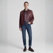 Load image into Gallery viewer, A model stands against a light gray studio background wearing a dark burgundy leather jacket over a patterned button-up shirt, blue jeans, and dark brown leather loafers.