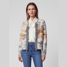 Load image into Gallery viewer, A woman modeling a cropped knit cardigan with abstract orange, gray, and cream patterns and fringe trim, worn over a cream blouse and blue jeans against a light gray studio background.