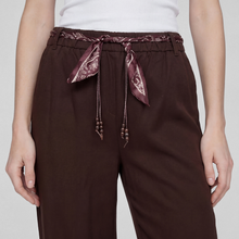 Load image into Gallery viewer, A close-up of a person wearing dark brown wide-leg trousers with a matching dark brown patterned waistband and drawstring tie, paired with a white top against a light gray studio background.