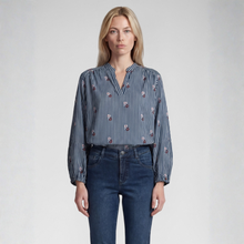 Load image into Gallery viewer, A woman modeling a long-sleeve button-up blouse with vertical navy and white stripes and small red floral accents, paired with dark blue jeans, against a light gray studio background.