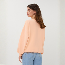 Load image into Gallery viewer, Woman wearing a peach blouse and blue jeans against a white background