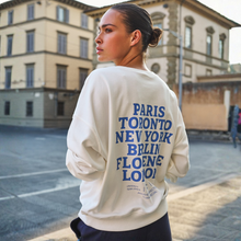 Load image into Gallery viewer, Person wearing a white sweatshirt with city names on the back, standing on a street.