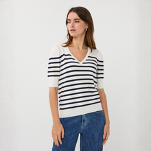 Load image into Gallery viewer, Woman wearing a white and navy striped sweater with blue jeans on a light gray background