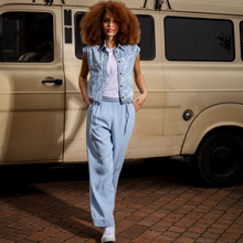 Load image into Gallery viewer, Woman in a light blue outfit standing in front of a vintage van on a brick road.
