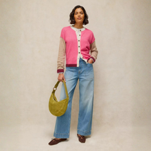 Load image into Gallery viewer, A model stands against a neutral beige studio backdrop wearing a pink and beige color-blocked cardigan over a white collared shirt, paired with wide-leg blue jeans and brown loafers, while holding a yellow-green crescent shoulder bag.