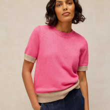 Load image into Gallery viewer, A woman wearing a bright pink short-sleeve crewneck sweater with beige ribbed trim at the cuffs and hem, paired with dark blue jeans, against a neutral beige background.