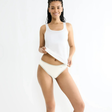 Load image into Gallery viewer, A woman modeling a white ribbed tank top and matching white bikini bottoms with a small gold beaded trim, posed against a solid white studio background.