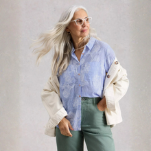 Load image into Gallery viewer, Woman wearing a light blue floral shirt over a white jacket with green pants against a plain background