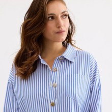 Load image into Gallery viewer, Woman wearing a blue and white striped shirt with decorative buttons on a plain background