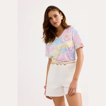 Load image into Gallery viewer, Woman wearing a colorful top and white shorts on a light background