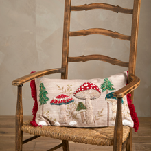 Load image into Gallery viewer, A decorative throw pillow with embroidered mushrooms and pine trees, draped over a rustic wooden ladder chair with a woven seat.