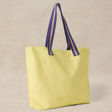 Load image into Gallery viewer, A light yellow canvas tote bag with purple woven shoulder straps featuring a beige stripe, set against a neutral beige background.