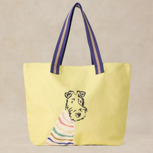 Load image into Gallery viewer, A light yellow canvas tote bag with dark purple handles featuring beige stripes, decorated with a black line art illustration of a dog wearing a rainbow-striped sweater, set against a neutral beige background.