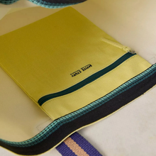 Load image into Gallery viewer, A close-up of a yellow fabric pouch or sleeve with a dark zipper, featuring the text 'KOREA STYLE' printed on it. The item is shown on a light beige background with a striped fabric strap visible at the bottom.
