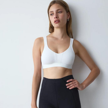 Load image into Gallery viewer, A woman wearing a white textured sports bra and black athletic leggings, posing against a plain light gray wall.