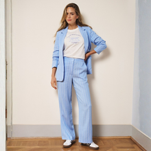 Load image into Gallery viewer, Model wearing the Esqualo Linen Trousers in a Pacific colour, with a wooden and white background.