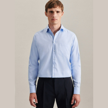 Load image into Gallery viewer, A man wearing a light blue long-sleeve button-down dress shirt with a single chest pocket, paired with dark trousers, standing against a neutral beige background.