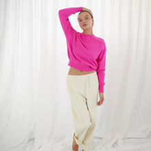 Load image into Gallery viewer, Person wearing a bright pink sweater and white pants against a white curtain background