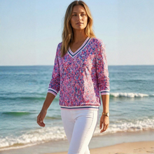 Load image into Gallery viewer, Woman wearing a colorful patterned shirt and white pants standing on a beach.