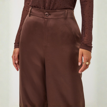 Load image into Gallery viewer, An up-close look at elegant coffee-toned trousers with a relaxed wide-leg cut and sleek, lustrous finish.