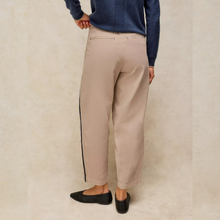 Load image into Gallery viewer, A person shown from the back wearing beige straight-leg trousers with a thin black side stripe, a navy blue sweater, and black flats, standing against a textured beige studio backdrop.