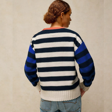 Load image into Gallery viewer, A woman viewed from behind wearing a striped knit sweater with navy, white, and royal blue horizontal stripes, paired with light blue jeans, against a neutral beige background.