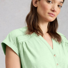 Load image into Gallery viewer, A close-up of a woman wearing a light mint green short-sleeve blouse with a V-neck and decorative buttons, set against a neutral gray background.
