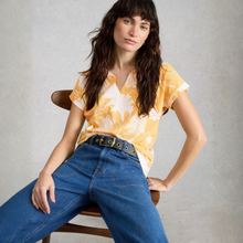 Load image into Gallery viewer, Woman wearing a yellow floral top and blue jeans sitting on a chair against a gray background