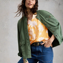 Load image into Gallery viewer, Woman wearing a green jacket over a yellow floral top and blue jeans against a gray background