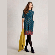 Load image into Gallery viewer, Woman wearing a patterned dress holding a yellow scarf against a plain background