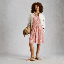 Load image into Gallery viewer, Woman wearing a red patterned dress with a beige jacket and sandals, holding a straw bag against a plain background.