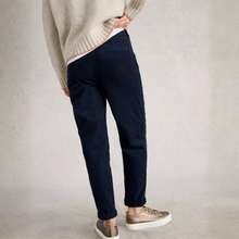 Load image into Gallery viewer, A person shown from the back wearing dark navy slim-fit jeans, a cream ribbed knit sweater, and beige sneakers against a textured light gray studio wall.