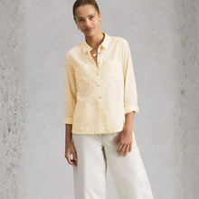 Load image into Gallery viewer, Woman wearing a light yellow shirt and white pants against a gray textured wall