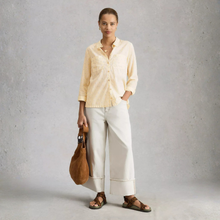 Load image into Gallery viewer, Woman wearing a light yellow shirt and white pants, holding a brown leather bag against a gray background