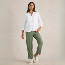 Load image into Gallery viewer, Woman wearing a white shirt and green pants against a beige background
