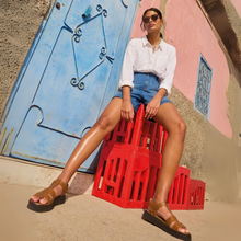 Load image into Gallery viewer, Woman sitting on a red crate against a colorful wall.