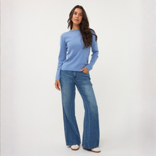 Load image into Gallery viewer, A woman modeling a light blue long-sleeve knit sweater and wide-leg blue jeans against a plain white studio background.
