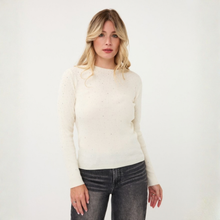 Load image into Gallery viewer, A woman modeling a cream-colored long-sleeve knit sweater with tiny speckled details, paired with dark gray jeans, against a plain white studio background.
