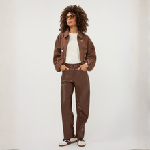 Load image into Gallery viewer, A model with curly hair wearing a brown cropped jacket, matching brown pants, a white top, and white sneakers with black stripes, standing against a light gray studio background.
