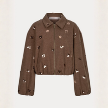 Load image into Gallery viewer, A cropped brown jacket with a full front zipper, pointed collar, and scattered sequined flowers in gold, silver, and black, displayed against a light off-white background.
