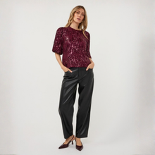 Load image into Gallery viewer, A woman modeling a short-sleeve burgundy sequined top paired with black wide-leg trousers and burgundy heels, standing against a plain light gray studio background.
