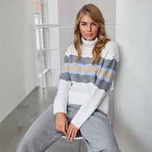 Load image into Gallery viewer, A woman sits on a chair in a bright indoor setting, wearing a fuzzy white turtleneck sweater with horizontal gray, beige, and light blue stripes, paired with gray sweatpants.
