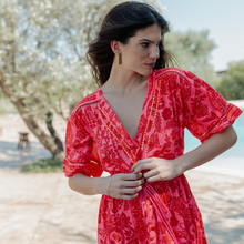 Load image into Gallery viewer, Woman in a red dress standing by a pool with trees in the background
